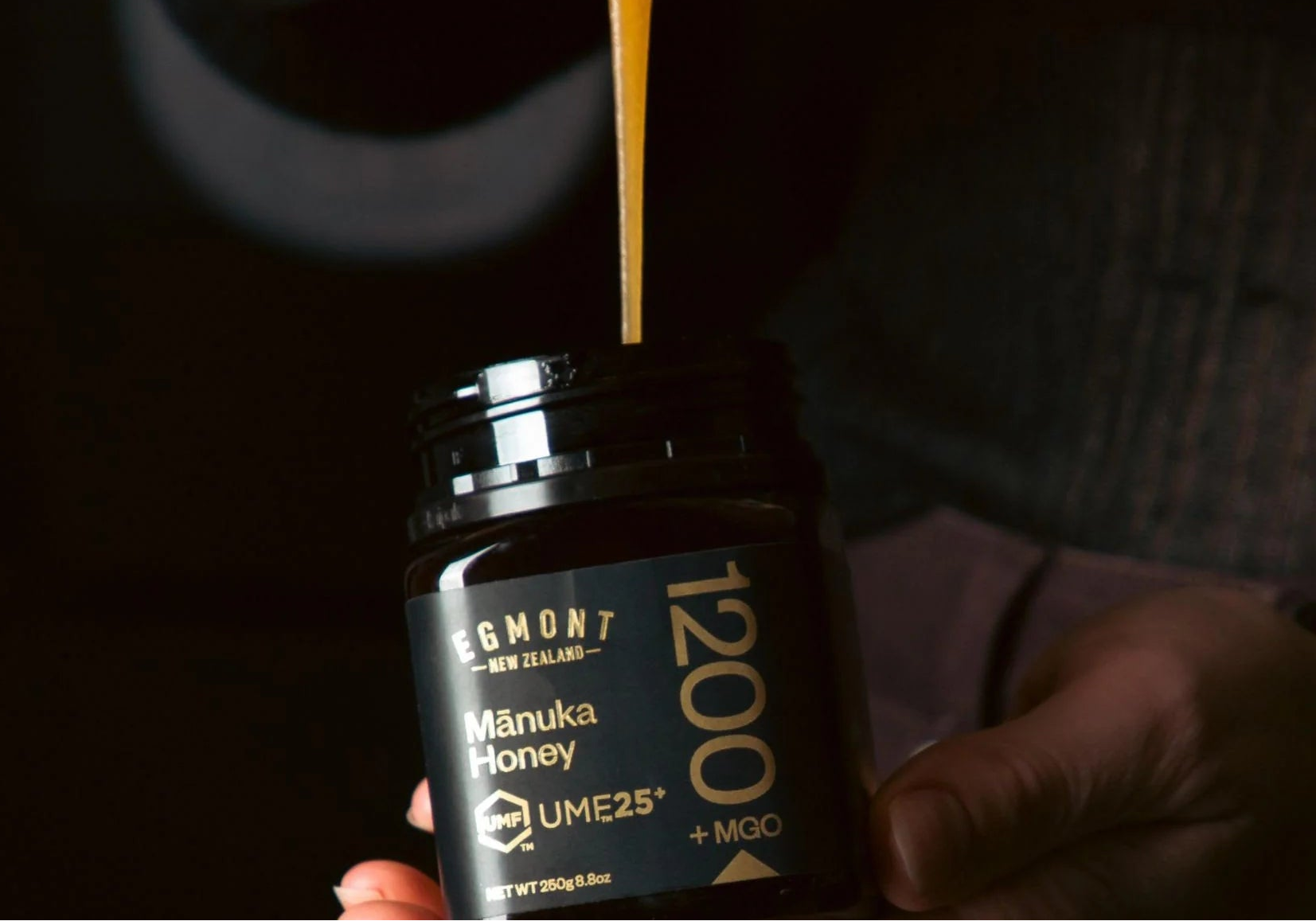 Man holding a jar of Māori Honey with honey dripping from a spoon