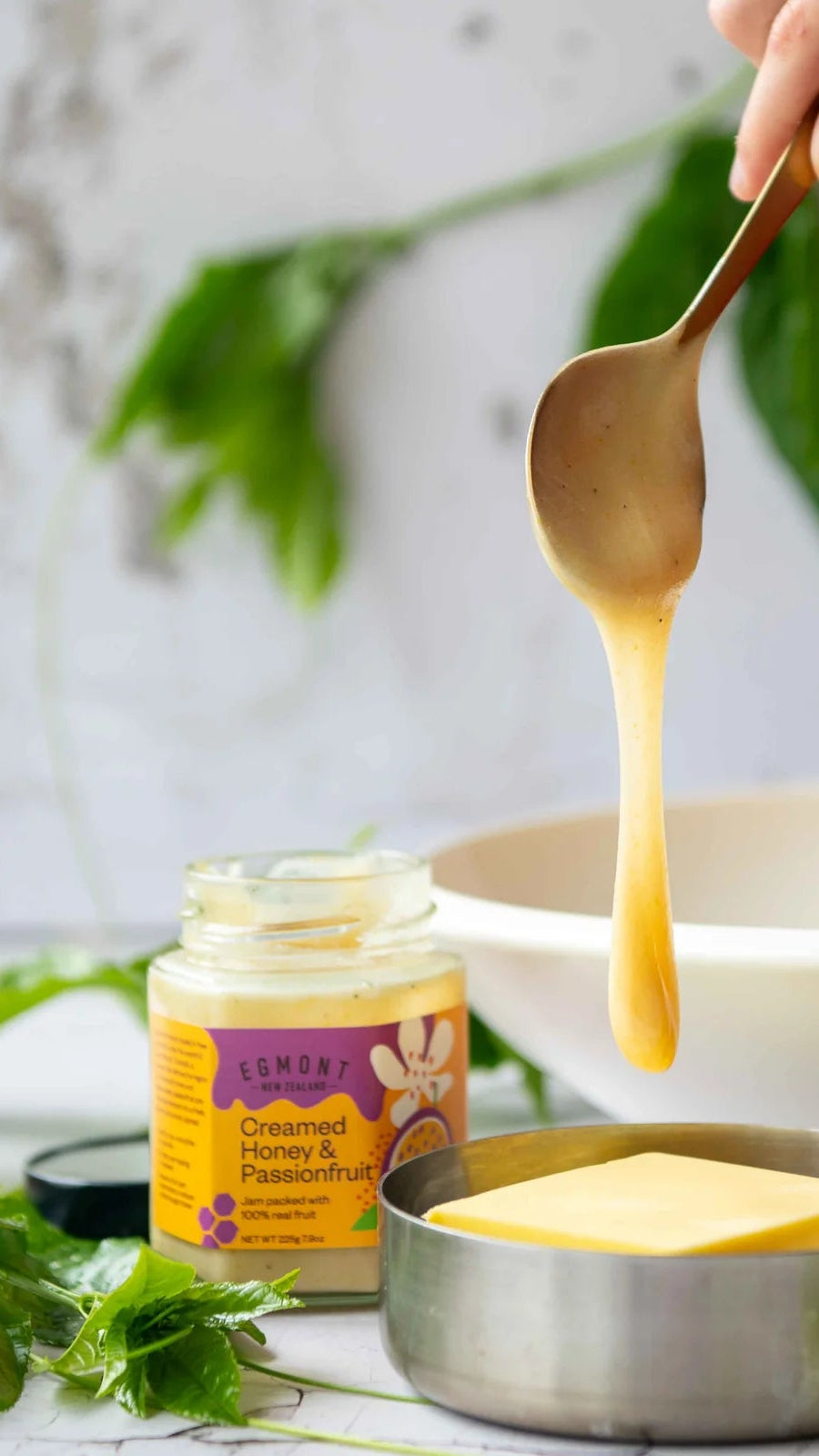 Hand holding a spoon with honey over a bowl, jar of honey in the background
